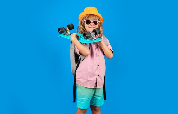 Photo of little child boy hold skateboard isolated on blue background casual culture child with skateboard and fashion stylish clothes in studio