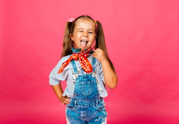 ピンクの背景に孤立して立っている、サングラスをかけて、カメラを見ている小さなかわいい美しい少女の写真。