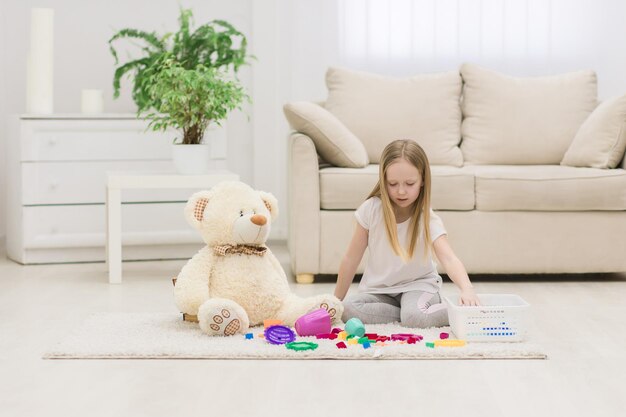 Photo of little girl playing with teddy bear sitting on the floor