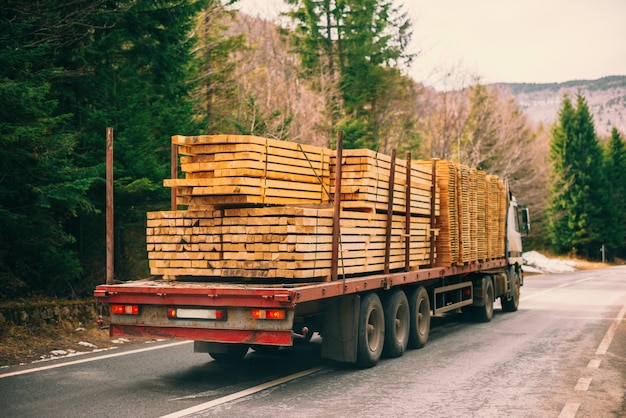 道路で木材を運ぶ長いトラックの写真。