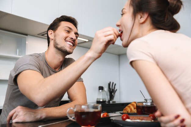 フラットでテーブルに座って、一緒に朝食を食べている愛情のあるカップルの男性と女性の写真