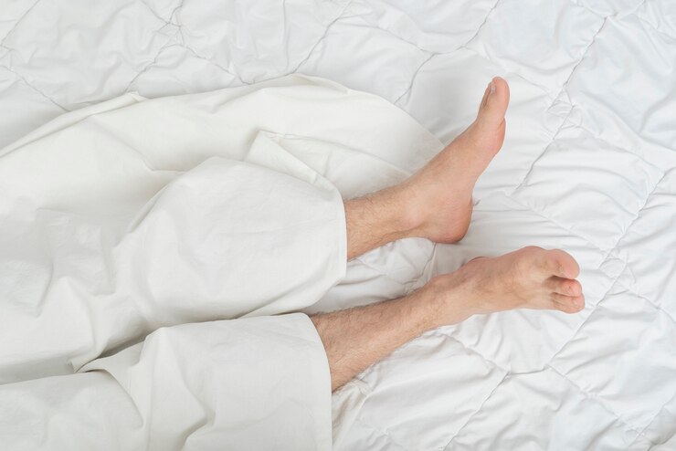 Photo of male feet on the bed under the sheet. Top view. Man sleeping on bed under blanket.