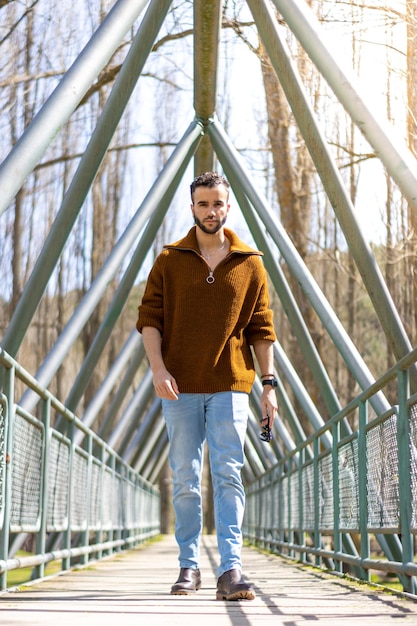 Photo of a man in a brown sweater walking on a bridge