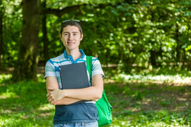 Photo of man in glasses with laptop, and backpack in summer park