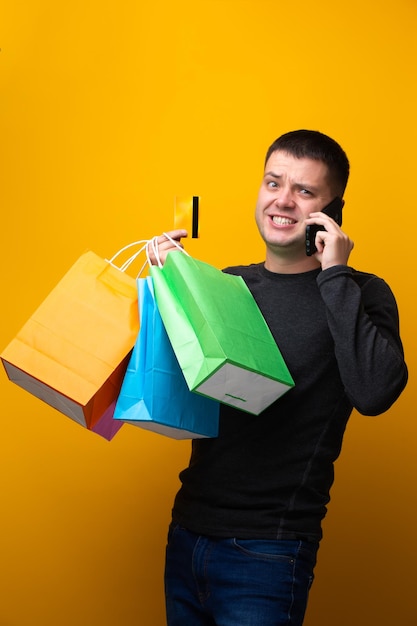 Photo of man shopper with paper bags bank card and phone in hand