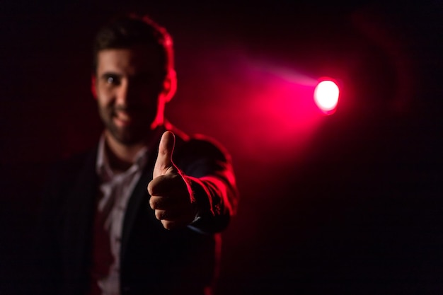 Photo of man showing thumb up on dark background with pink light