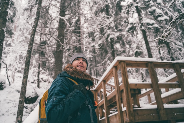 Photo of man in winter forest on wooden bridge