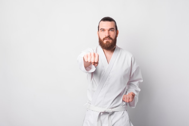 Photo of man with beard wearing taekwondo uniform training over white wall
