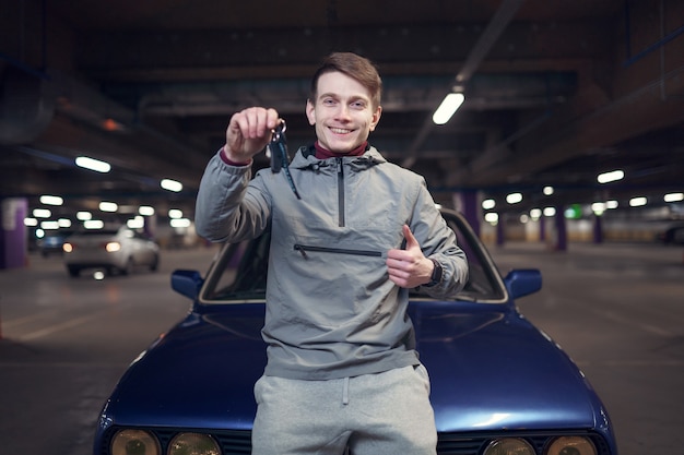 Photo of man with keys standing by car in underground parking