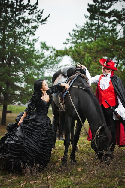 Photo of man and woman in a beautiful theater costumes riding in the woods