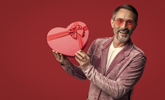 Photo photo of mature man showing valentine gift mature man with valentine gift isolated on red