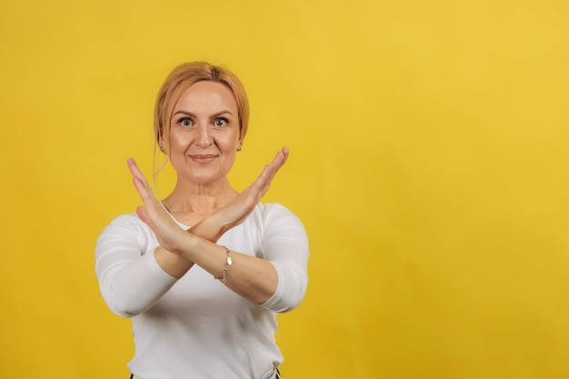 Photo of mature pretty serious woman crossed hands show no stop\
forbidden symbol isolated over yellow color background