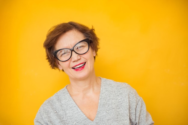 Photo of mature smiling positive woman in glasses isolated on yellow color background