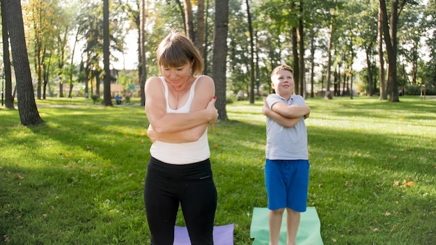 Photo of middle aged mother with her teenage boy child doing yoga and breathing exercises at park. Family taking care of thir mental and physical health while doing sports