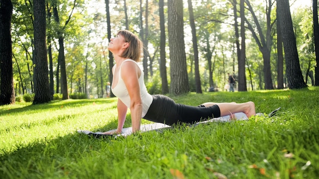 Photo of middle aged smiling woman practising yoga asana. Persong meditating in nature. Balance and harmony of body and mind