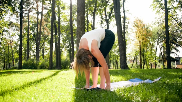 Photo of middle aged woman in sportrs clothes practicing yoga outdoors at park. Middle aged woman stretching and meditating at forest