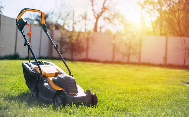 Foto di una falciatrice da giardino elettrica moderna che si leva in piedi su un prato inglese del cortile vicino a una casa