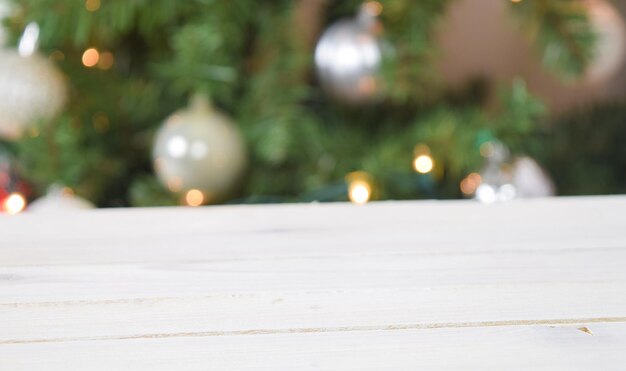 Photo of modern white wood tabletop in front of a festive Christmas tree with glowing white lights