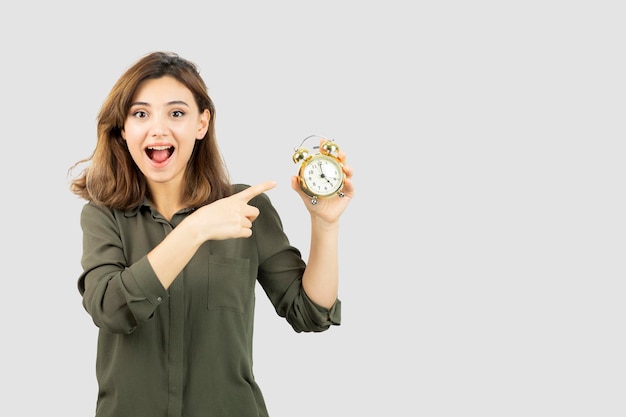 Photo of morning girl holding alarm clock over white wall. High quality photo