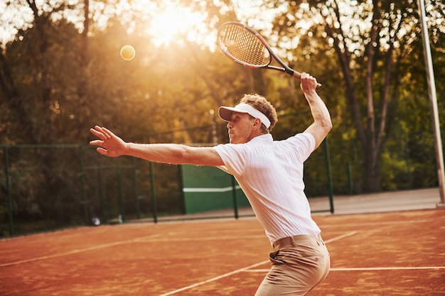Foto in movimento. il giovane tennista in abiti sportivi è in campo all'aperto.