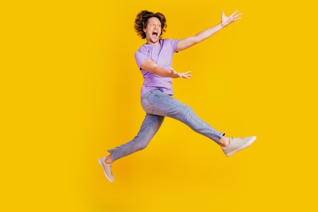 Фото красивого вдохновленного человека прыгать, поднимать руки, пустое место, идти носить повседневную джинсовую одежду на желтом фоне