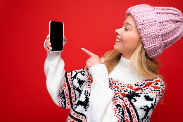 Фото Фото привлекательной улыбающейся молодой блондинки в теплой вязаной шапке и зимнем теплом свитере