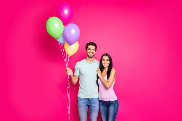 熱気球を手に持っている魅力的な男と女のカップルの写真は、両親の誕生日パーティーを着てカジュアルな服装の孤立したピンク色の背景に来ました