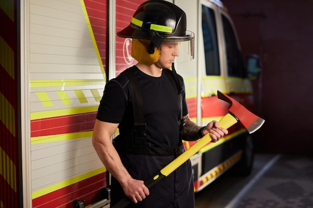 写真 消防車に対して斧でヘルメットをかぶっている消防士の写真