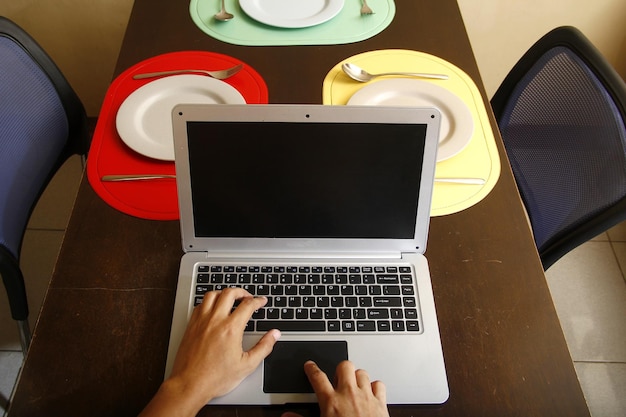 Фото Фото ноутбука с руками, печатающими на нем тарелки и посуду на обеденном столе