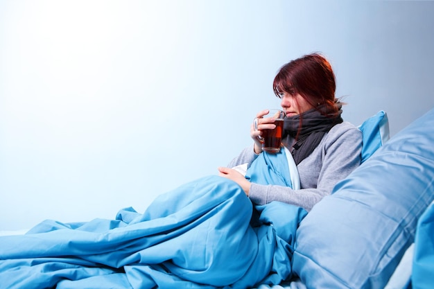 Фото Фото больной брюнетки с чашкой чая, сидящей в постели