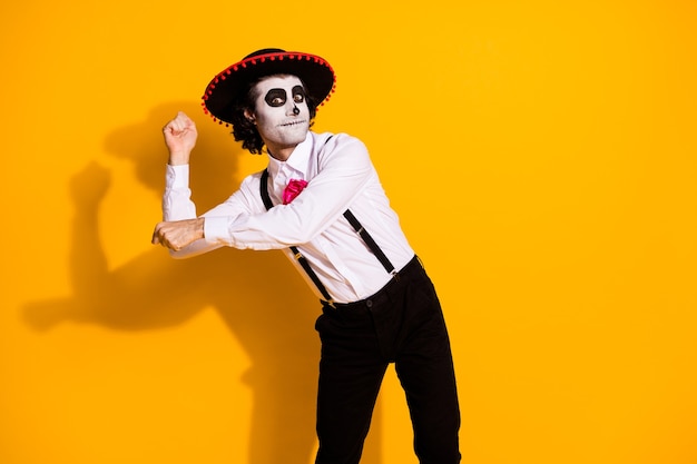 Фото жуткий призрак монстр парень танцует латиноамериканский национальный танец притвориться провести фестиваль маракасов парень носить белую рубашку роза смерть костюм подтяжки сомбреро изолированный желтый цвет фона