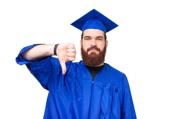 Фото Фотография студента с бородой в синем халате, показывающего неприязнь, большой палец вниз