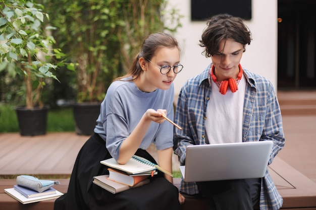 写真 本を持ってベンチに座って、大学の中庭でラップトップで作業している2人の学生の写真