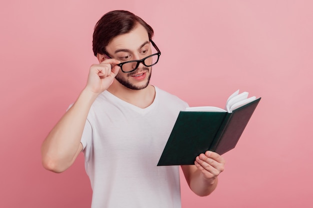 Фото Фото молодого красивого человека счастливой позитивной улыбкой читать книгу руки сенсорные очки, изолированные на розовом цветном фоне