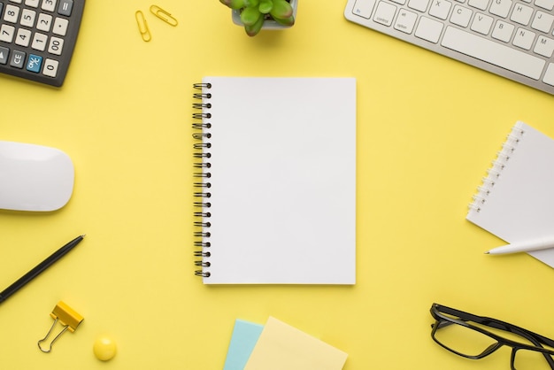 Photo overhead of notebook keyboard calculator pen computer mouse notes plant glasses and paperclips isolated bright color yellow backdrop