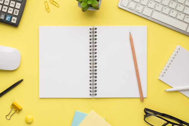 Photo overhead of notebook keyboard calculator pen pencil computer mouse notes plant glasses and paperclips isolated on the yellow background