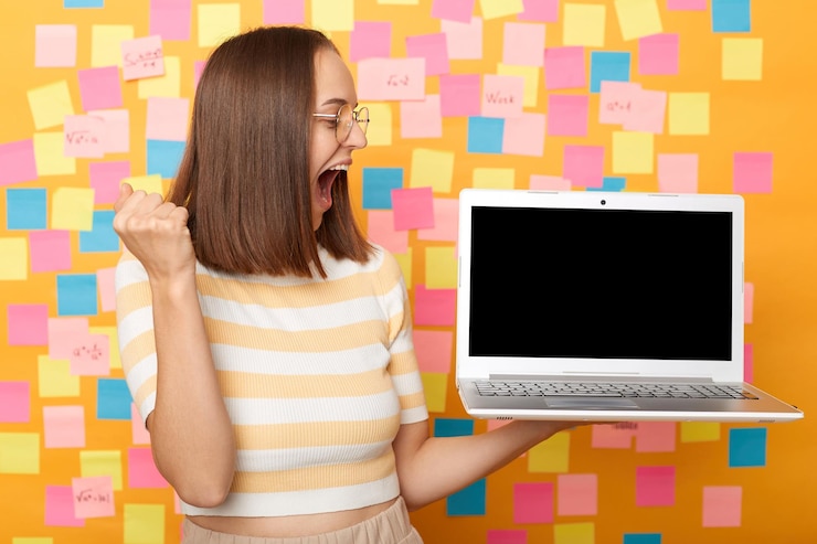 फोटो photo of overjoyed happy joyful brown haired woman wearing tshirt looking at empty display for advertisement clenched fist celebrating posing against colorful sticky notes on yellow wall