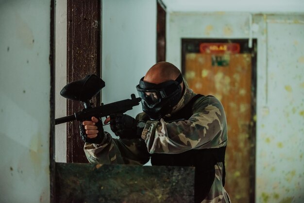 Photo photo of paintball player in goggle mask and camouflage aiming by paintball gun selective focus