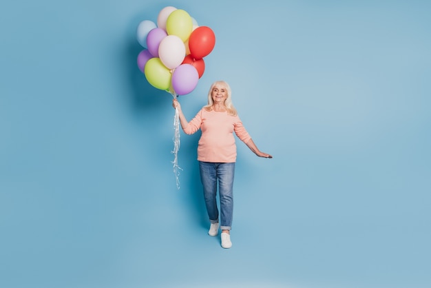 Photo of pensioner dreamy woman hold many air baloons in pink sweater on blue background