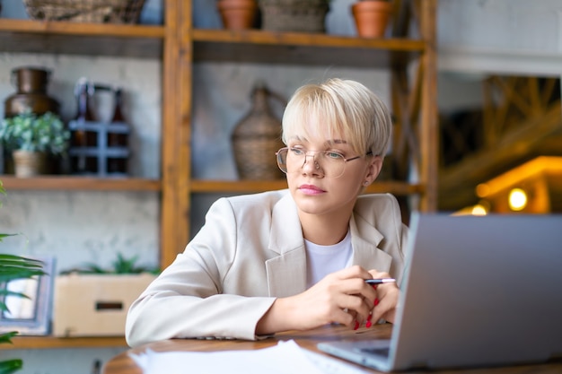 Photo of a pensive woman in front of a laptop monitor she works with documents and papers at home  c...