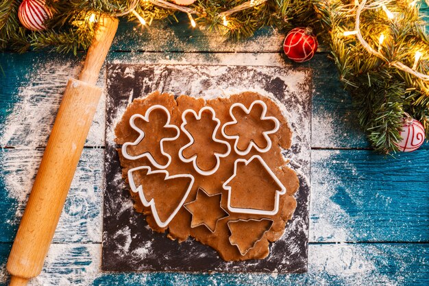 Photo of pine branches, dough, biscuit molds, rolling pin on blue wooden table