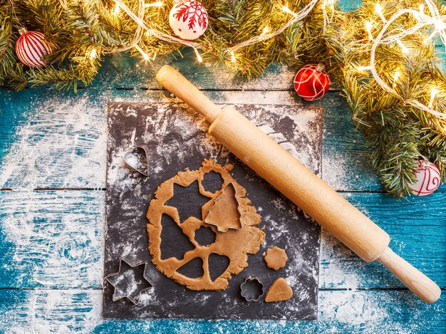 Photo of pine branches, dough, biscuit molds, rolling pin on blue wooden table