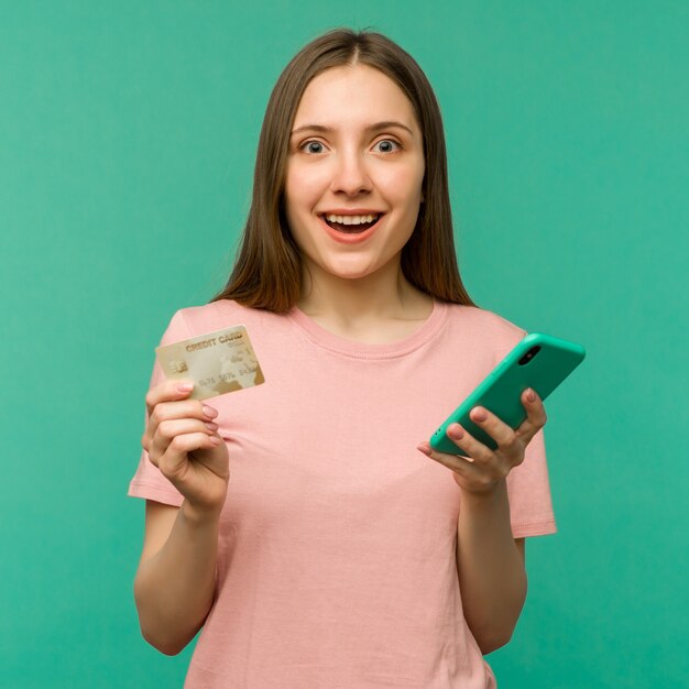 Foto foto di felice felice urlando giovane donna in posa isolato su sfondo blu muro utilizzando il telefono cellulare in possesso di carta di credito.