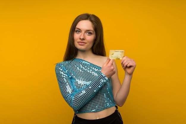 Photo of pleased young woman posing isolated over yellow wall background holding debit or credit card.