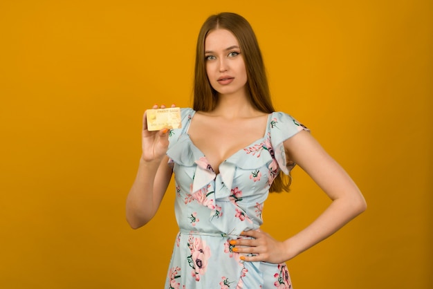 Photo of pleased young woman posing isolated over yellow wall background holding debit or credit card.