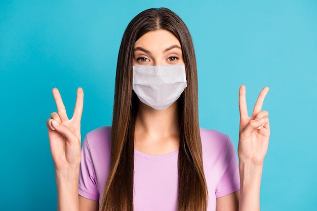 Photo portrait of adorable woman showing two v-signs wearing white face mask isolated blue color background