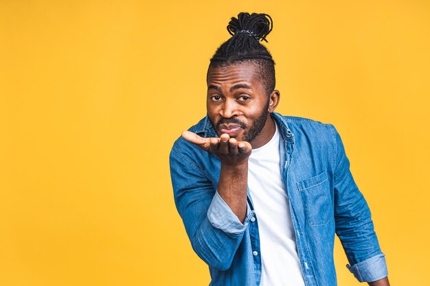 Photo portrait of african american black man sweet romantic sending air kiss to copyspace isolated over yellow background.