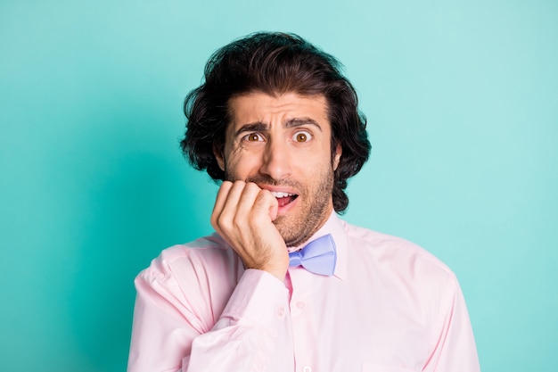 Photo portrait of anxious man biting nails isolated on pastel cyan colored background