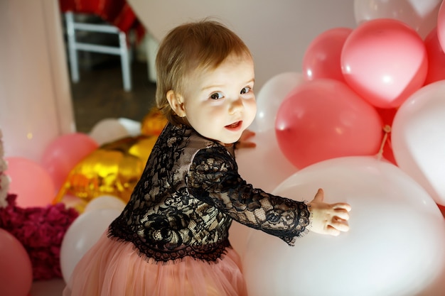 Ritratto fotografico di una ragazza di compleanno di 1 anno in un abito rosa con palloncini rosa. il bambino in vacanza sorride, le emozioni dei bambini. festa di compleanno