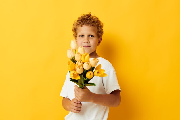 Photo portrait curly little boy with a bouquet of yellow flowers color background unaltered